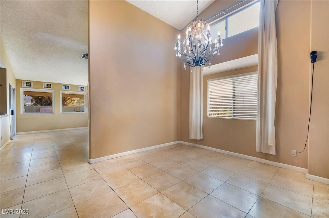 300 Redondo Street Henderson, NV 89014 - Photo 9 of 29 Unfurnished dining area with a chandelier, light tile patterned flooring, high vaulted ceiling, and a textured ceiling