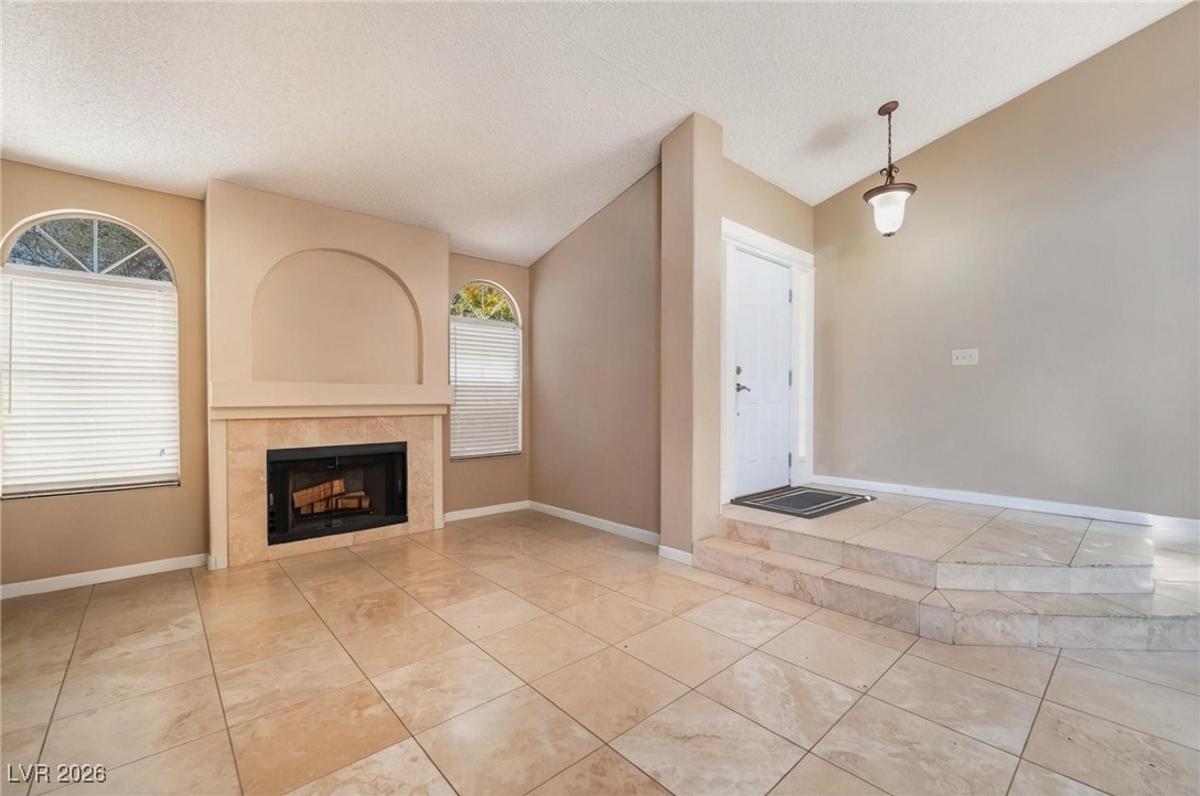 300 Redondo Street Henderson, NV 89014 - Photo 10 of 29 Unfurnished living room with lofted ceiling, a fireplace, a textured ceiling, and light tile patterned floors