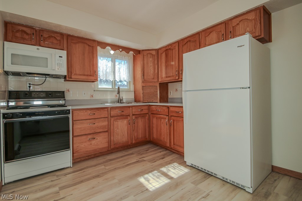 30224 Regent Road Wickliffe, OH 44092 - Photo 5 of 27 Kitchen featuring white appliances, wood finish cabinetry, light countertops, light wood finished floors, and decorative backsplash