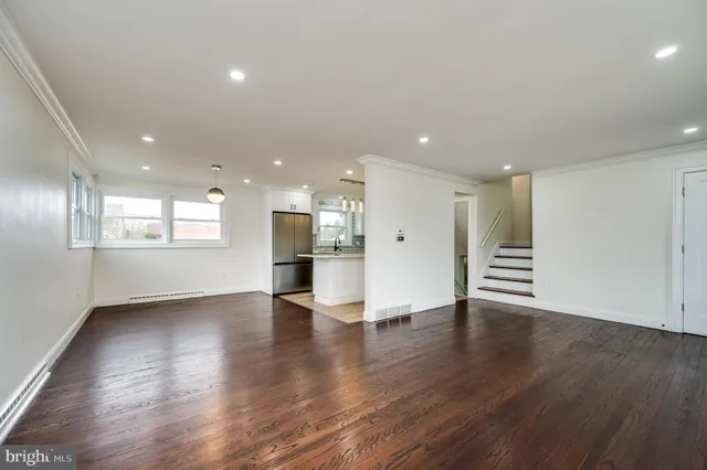 a view of an empty room with wooden floor and a kitchen