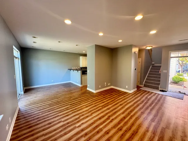 a view of an empty room with wooden floor and a kitchen