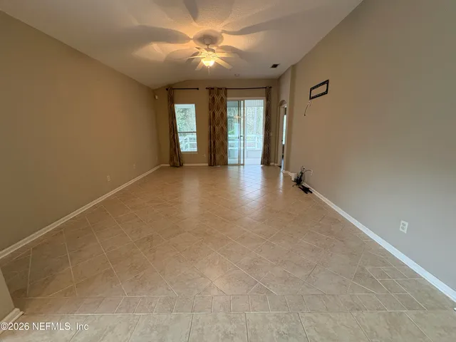 an empty room with chandelier fan and windows