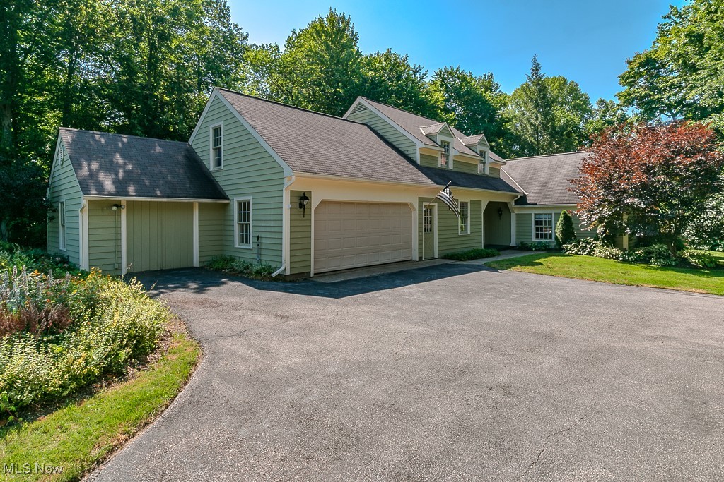 View of front of house with a garage, asphalt driveway, and roof with shingles