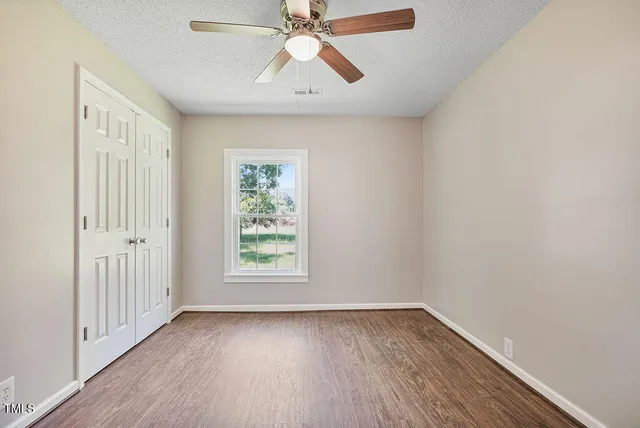 an empty room with wooden floor chandelier fan and windows