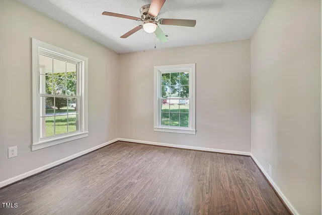 an empty room with wooden floor fan and windows