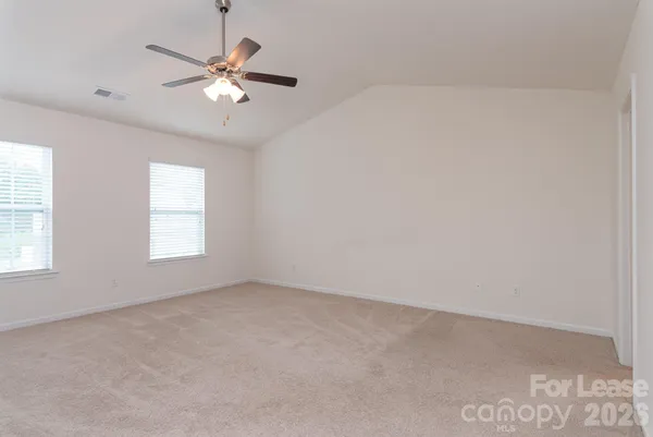 an empty room with chandelier fan and windows