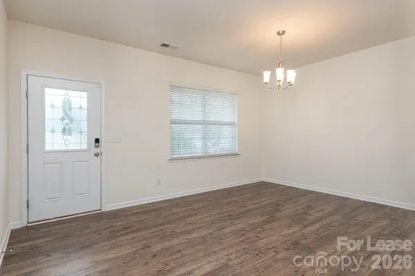 an empty room with wooden floor chandelier and windows