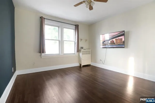 an empty room with wooden floor chandelier fan and windows