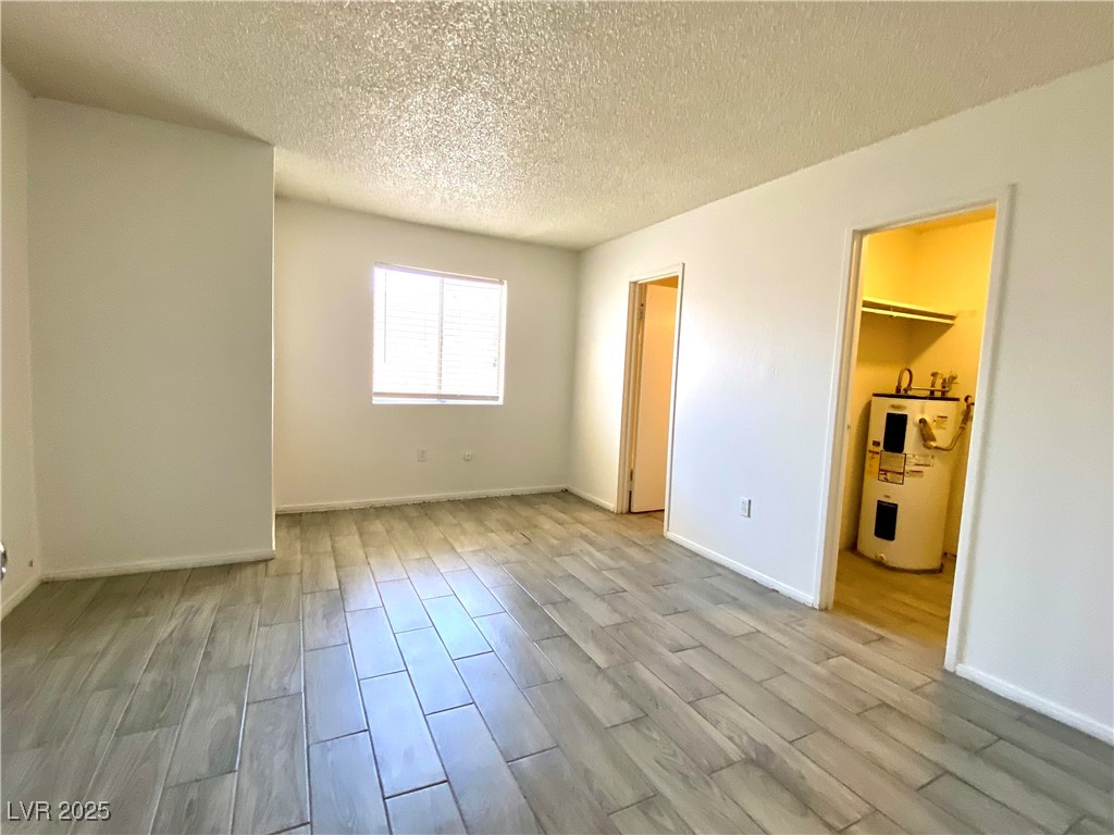 6213 Smoke Ranch Road Las Vegas, NV 89108 - Photo 13 of 22 Unfurnished bedroom with light wood-type flooring, a textured ceiling, and water heater