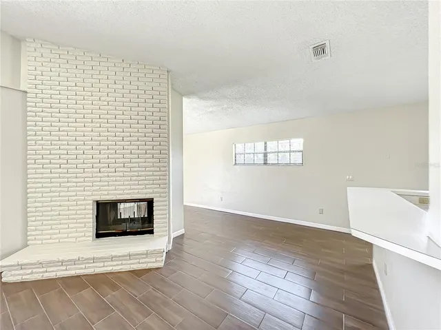 a view of an empty room with wooden floor and a fireplace