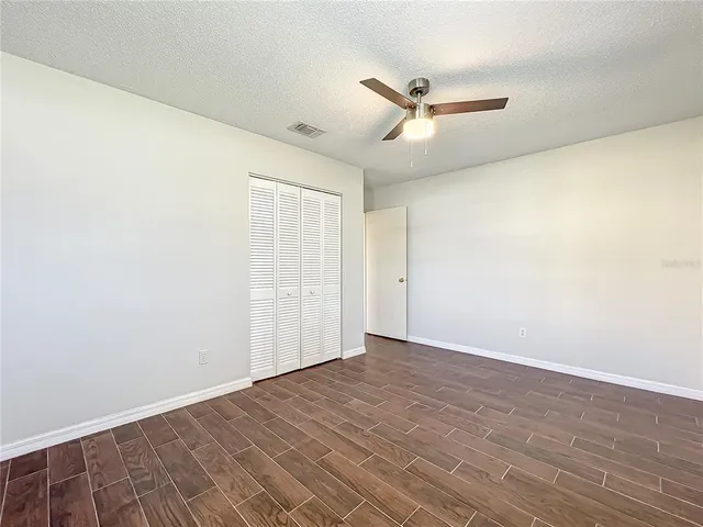 an empty room with wooden floor fan and windows
