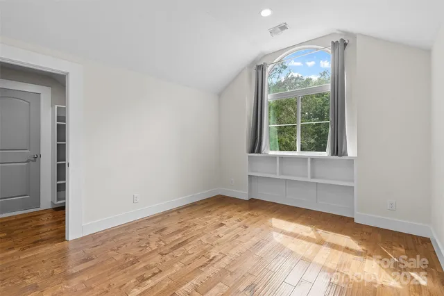 an empty room with wooden floor cabinet and windows