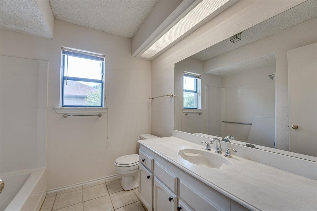 3410 Conlin Drive Rowlett, TX 75088 - Photo 16 of 27 a bathroom with a granite countertop toilet a sink and mirror