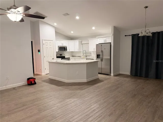 a view of kitchen with stainless steel appliances granite countertop a sink dishwasher a refrigerator and a dining table with wooden floor