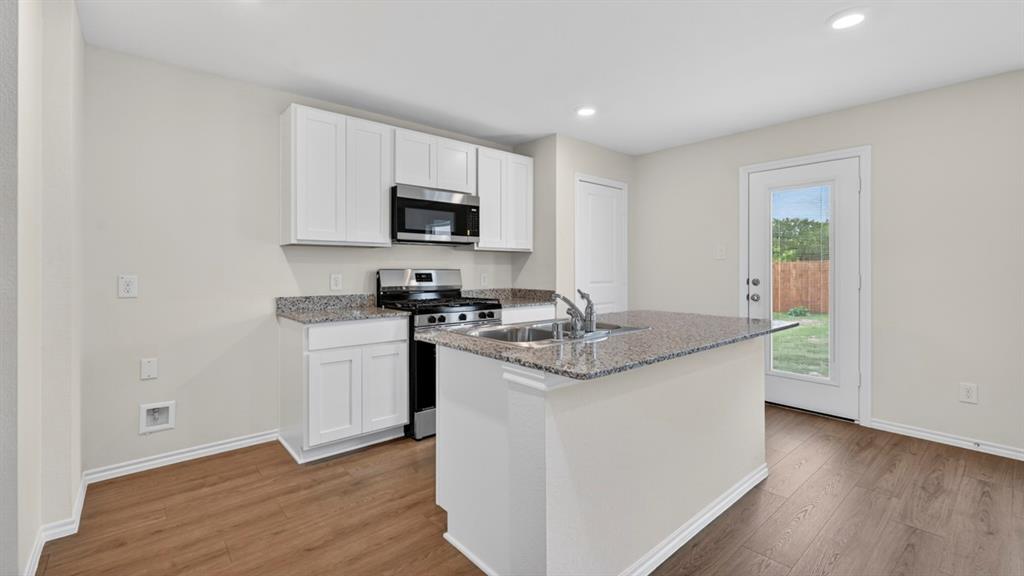 3534 Spring Time Street Forney, TX 75126 - Photo 2 of 24 Kitchen featuring a central island with an undermount sink and a stainless steel faucet, wood-finish flooring, white cabinetry, stainless steel appliances, and recessed lighting