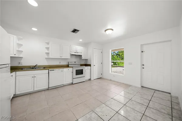 a large white kitchen with granite countertop white cabinets stainless steel appliances a sink and a window