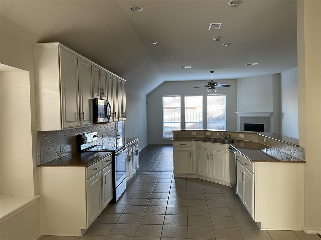 1133 Elm Grove Drive Allen, TX 75002 - Photo 4 of 11 Kitchen featuring stainless steel appliances, decorative backsplash, vaulted ceiling, white cabinetry, and light tile patterned floors