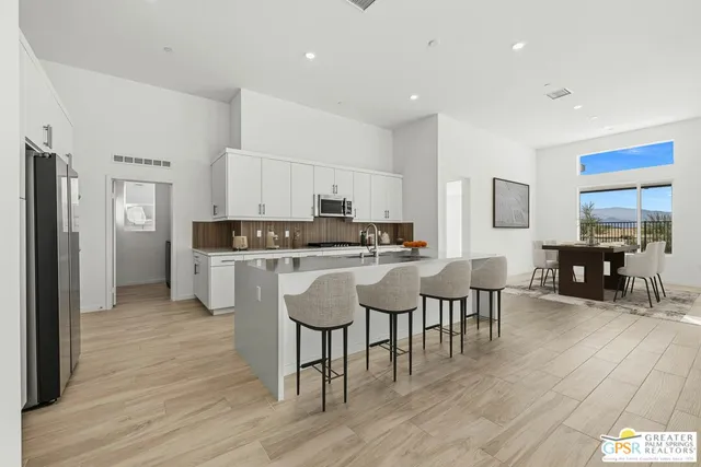 a open kitchen with stainless steel appliances granite countertop a stove a refrigerator a kitchen island a dining table and chairs with wooden floor