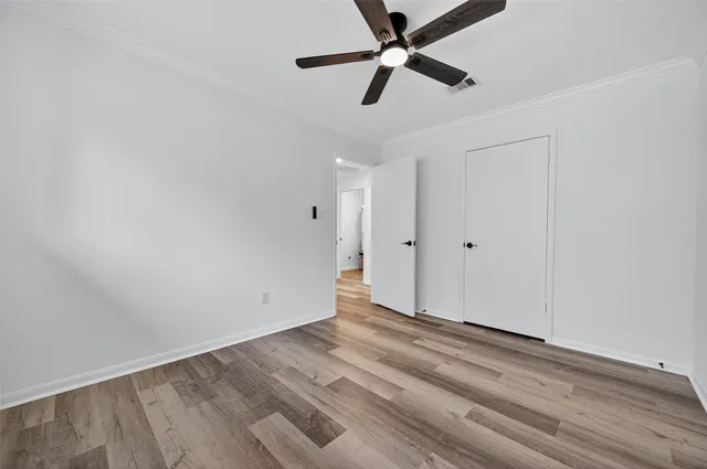 an empty room with wooden floor ceiling fan and windows