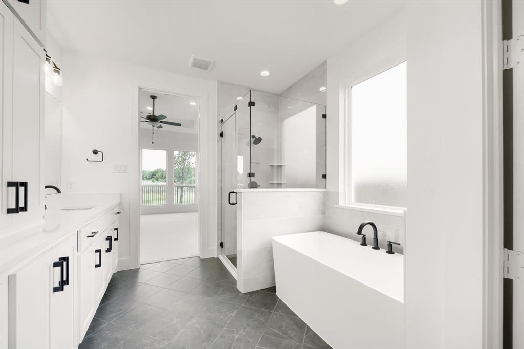 733 Red Cedar Road Haslet, TX 76052 - Photo 23 of 28 Spacious bathroom featuring a freestanding soaking tub with matte black fixtures, a walk-in shower with glass enclosure, dual vanity with white cabinetry and dark hardware, and dark tile flooring