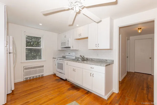 a kitchen with granite countertop a stove a sink and white cabinets with wooden floor next to windows