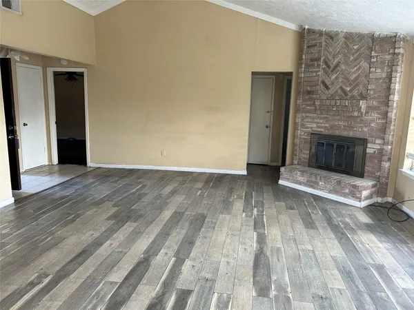 a view of an empty room with wooden floor fireplace and a window