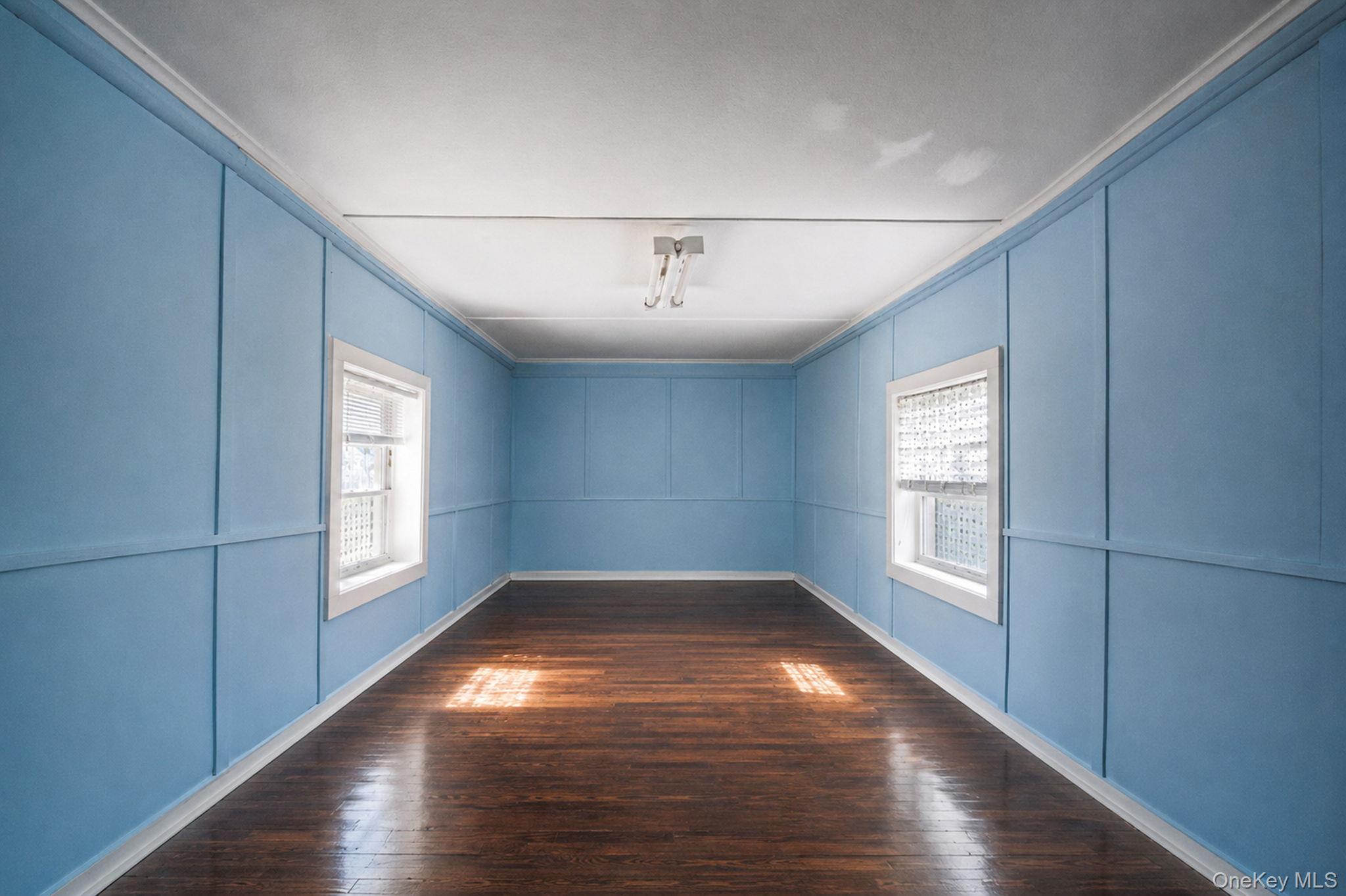 1055 Oregon Road Mattituck, NY 11952 - Photo 11 of 33 Room featuring wood-finish flooring, two windows with white trim, and light blue wall paneling