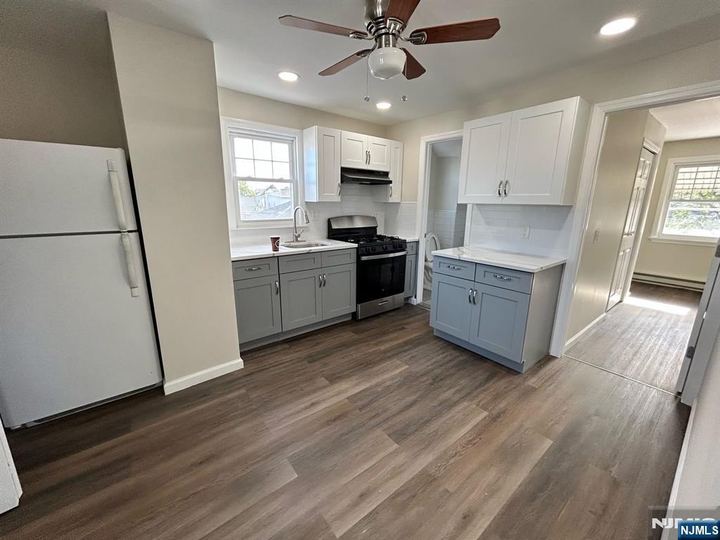 54 Windsor Street, Unit 3 Kearny, NJ 07032 - Photo 2 of 5 a large kitchen with a refrigerator a stove a microwave and white cabinets with wooden floor