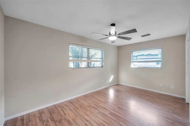 a view of an empty room with wooden floor and a ceiling fan