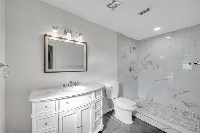 a bathroom with a toilet a sink a mirror a shower a vanity and window