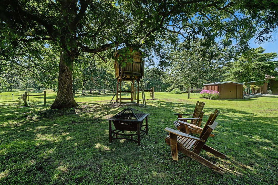 21019 Carter Road West Fork, AR 72774 - Photo 43 of 49 Expansive grassy yard featuring mature trees, a wooden treehouse structure, a storage shed, and a rustic fence line