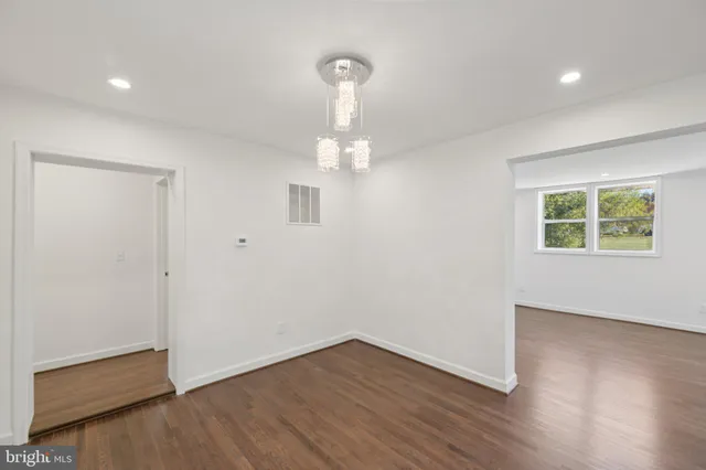 an empty room with wooden floor chandelier and windows