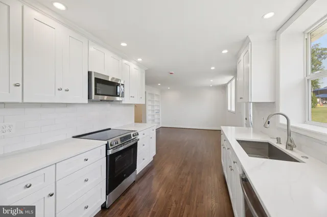 a kitchen with granite countertop a sink dishwasher stove and white cabinets with wooden floor