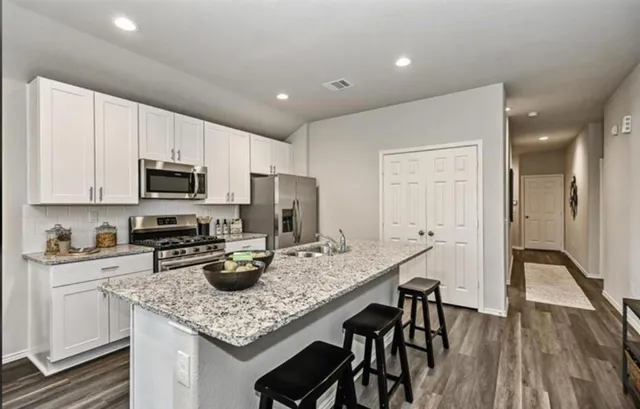 a kitchen with stainless steel appliances granite countertop a sink dishwasher a stove refrigerator and microwave with wooden floor