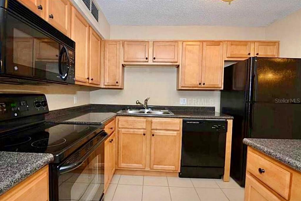 390 Woodside Drive, Unit 202 Altamonte Springs, FL 32701 - Photo 6 of 10 a kitchen with granite countertop a refrigerator stove and microwave