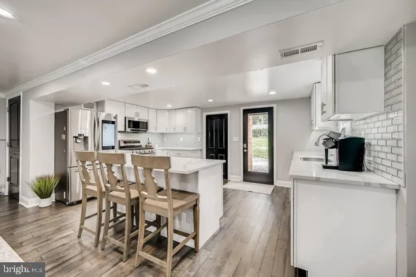 a kitchen with stainless steel appliances kitchen island granite countertop a refrigerator a stove top oven a sink dishwasher and white cabinets with wooden floor