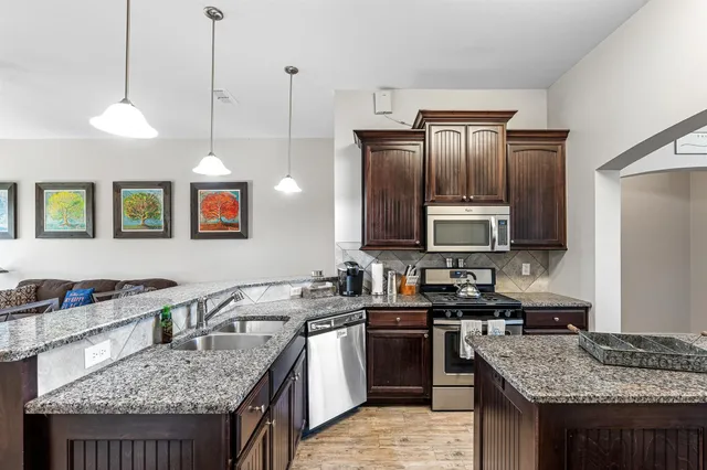 a kitchen with stainless steel appliances granite countertop a sink a stove and a wooden floor