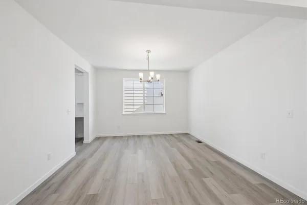 an empty room with wooden floor chandelier and windows