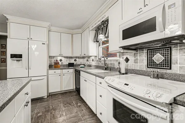a kitchen with granite countertop a sink stainless steel appliances and white cabinets