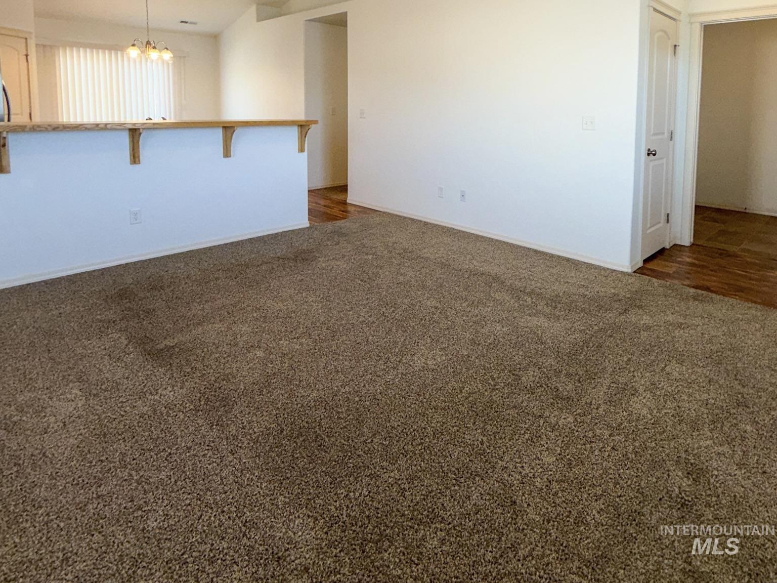 702 Emerald Street Rupert, ID 83350 - Photo 3 of 12 Empty room featuring dark colored carpet and a chandelier