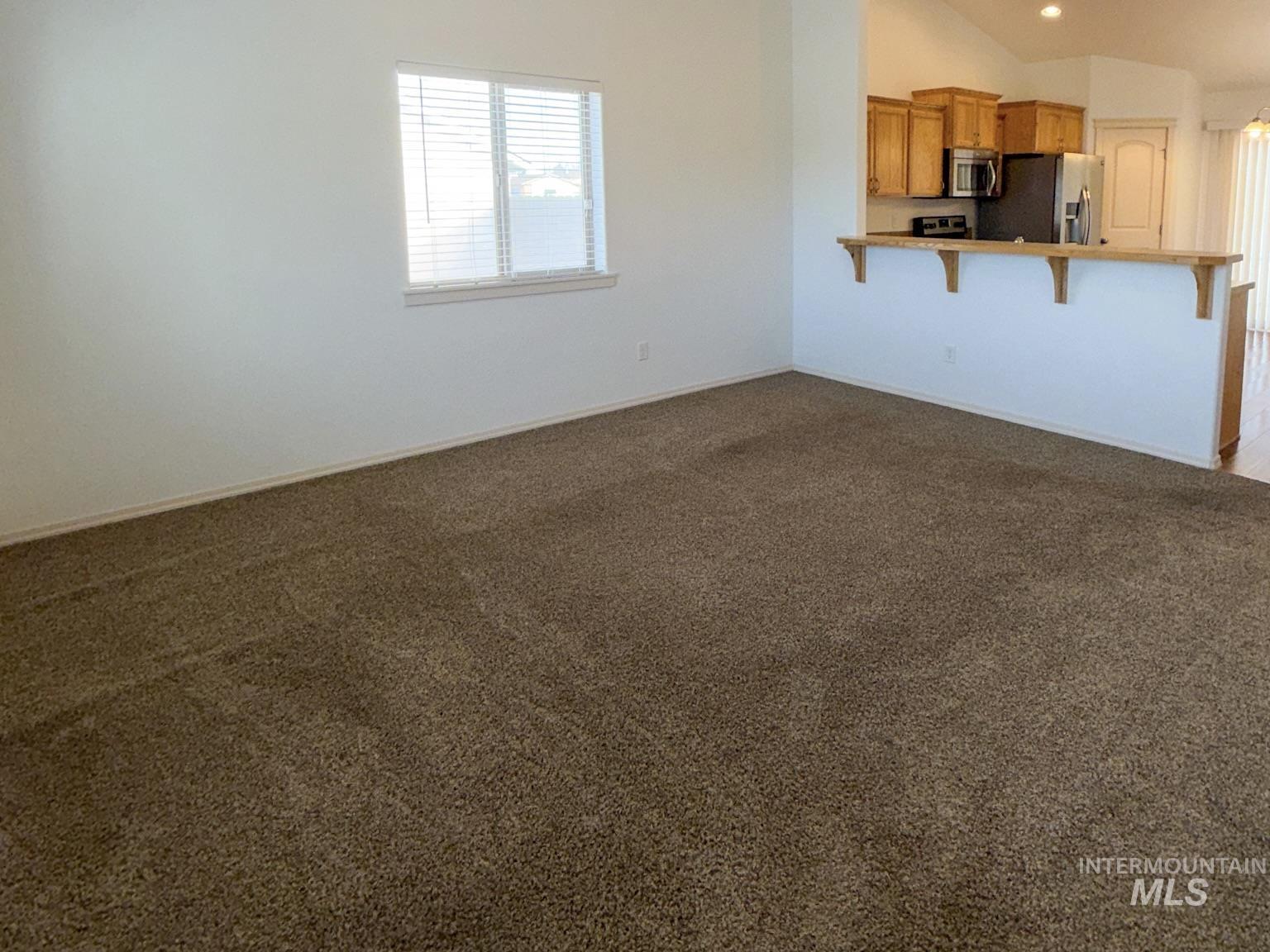 702 Emerald Street Rupert, ID 83350 - Photo 4 of 12 Unfurnished living room with dark colored carpet and lofted ceiling