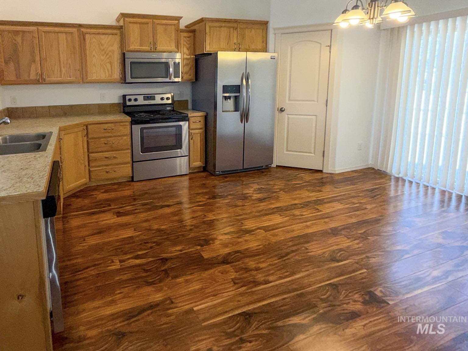 702 Emerald Street Rupert, ID 83350 - Photo 5 of 12 Kitchen with stainless steel appliances, light countertops, dark wood finished floors, a chandelier, and wood finish cabinets