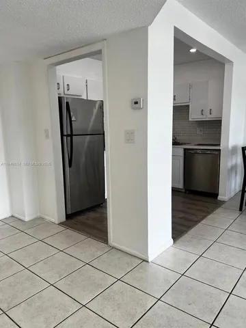 a view of a refrigerator in kitchen and an empty room in wooden floor