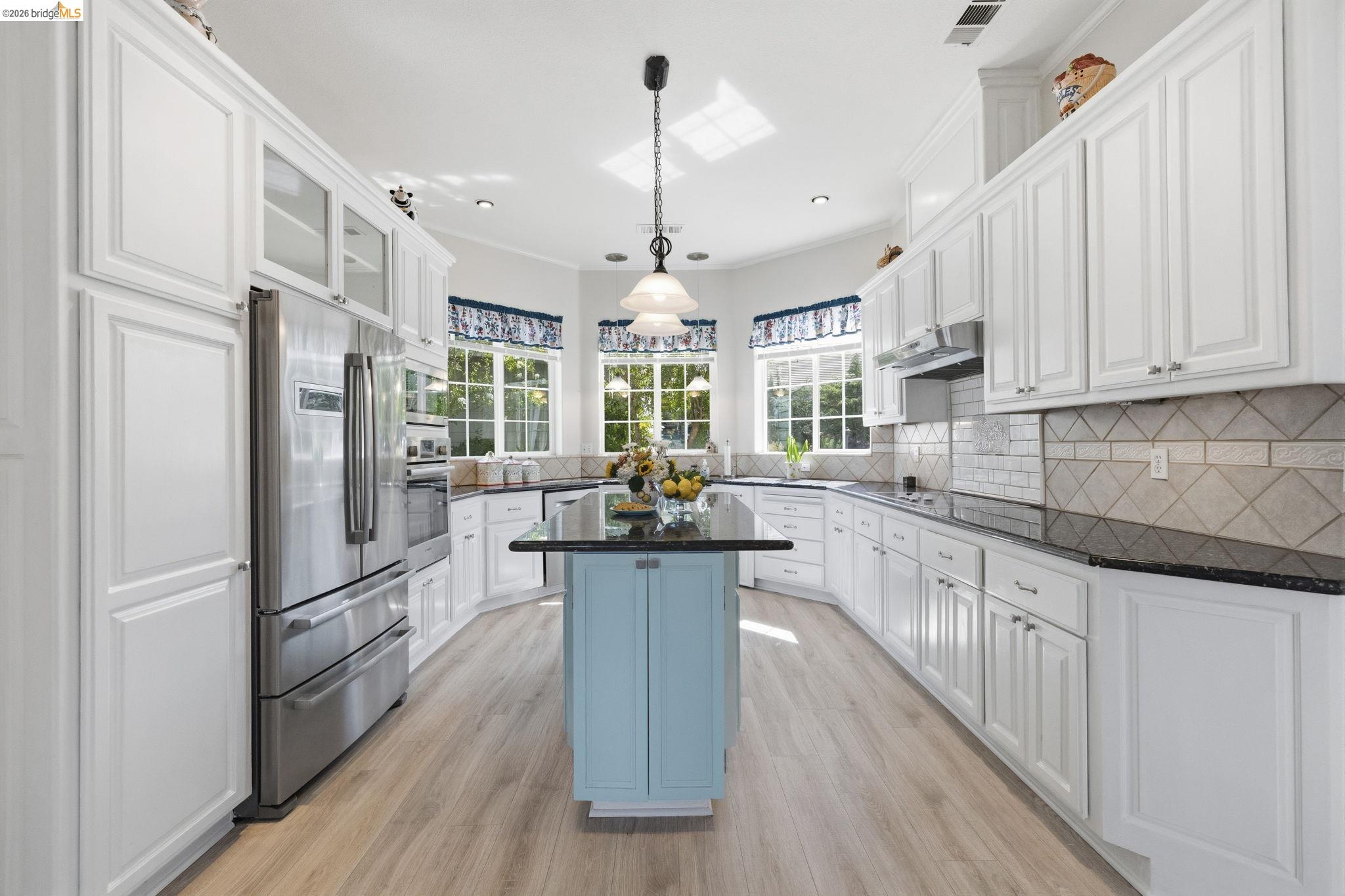 6242 Bluff View Road Copperopolis, CA 95228 - Photo 17 of 59 Bright kitchen featuring white cabinetry, black stone countertops, a light blue central island, light wood-finish flooring, and multiple windows