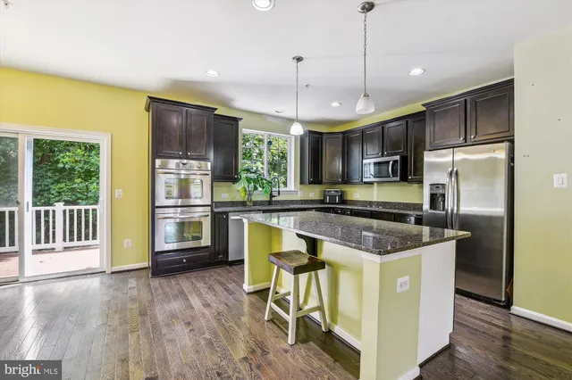 a kitchen with stainless steel appliances granite countertop a refrigerator a sink dishwasher a stove and a dining table with wooden floor