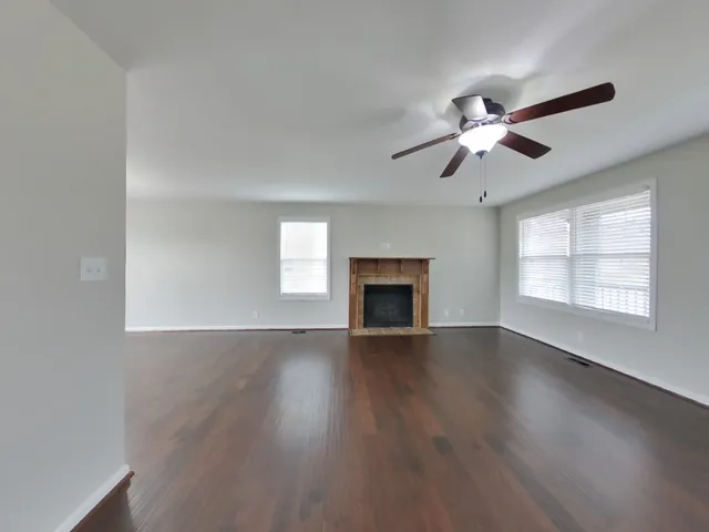 an empty room with wooden floor fan and windows