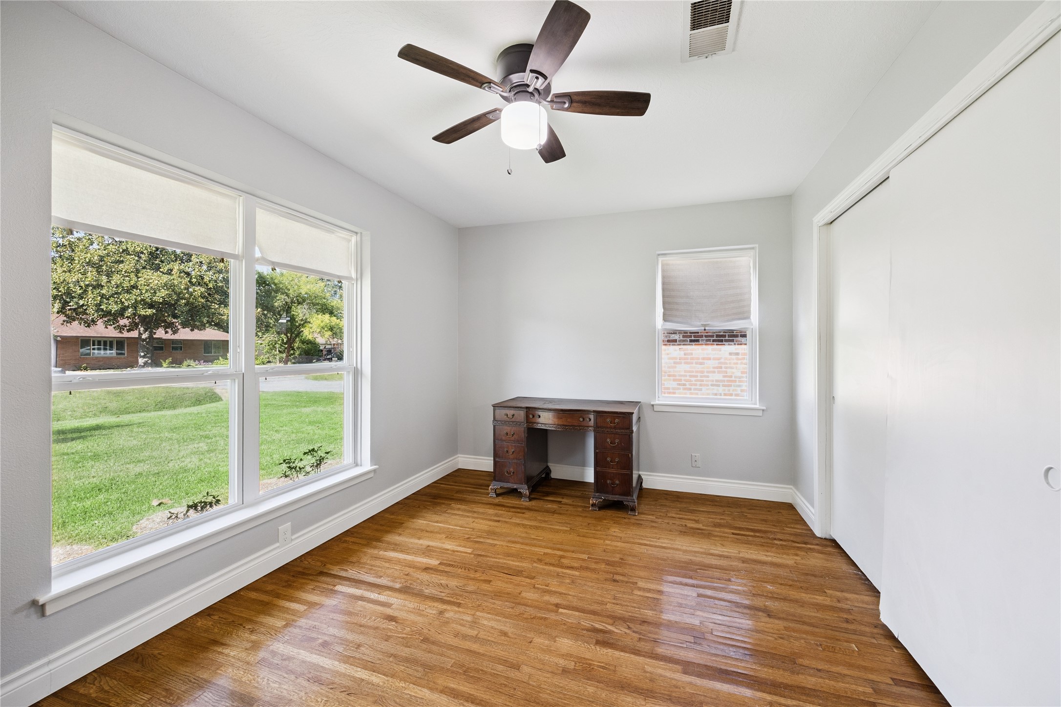 8911 Blankenship Drive Houston, TX 77080 - Photo 11 of 21 Bright bedroom with hardwood floors, large windows offering a view of the lawn, a ceiling fan, and a simple wooden desk. Perfect for a home office or cozy study space.
