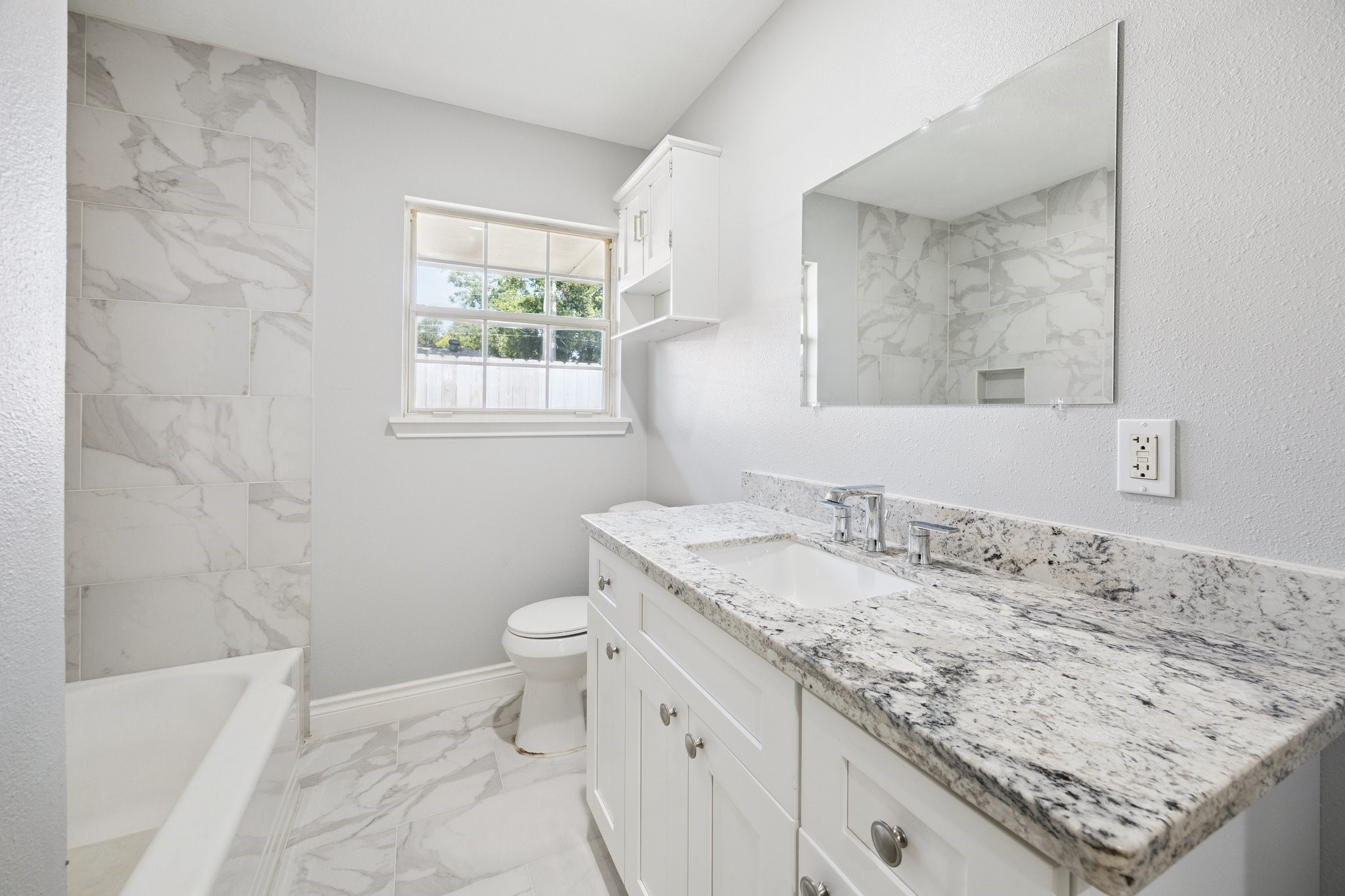 8911 Blankenship Drive Houston, TX 77080 - Photo 12 of 21 This bathroom features a sleek, modern design with a granite countertop, dual sinks, and a large mirror. It has a bright, airy feel thanks to the natural light from the window and the neutral color scheme, complemented by elegant marble tile in the shower area.