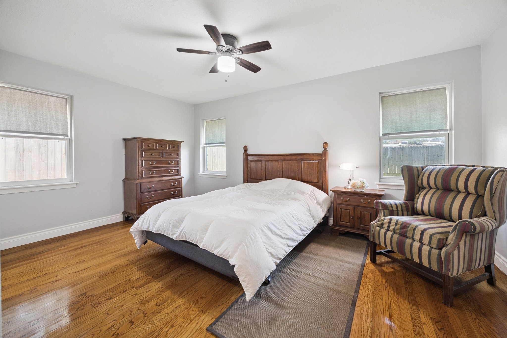 8911 Blankenship Drive Houston, TX 77080 - Photo 14 of 21 Primary bedroom is both bright and spacious, showcasing beautiful hardwood floors and a stylish ceiling fan. With natural light flowing through three large windows, it creates a warm and refreshing atmosphere perfect for relaxation.