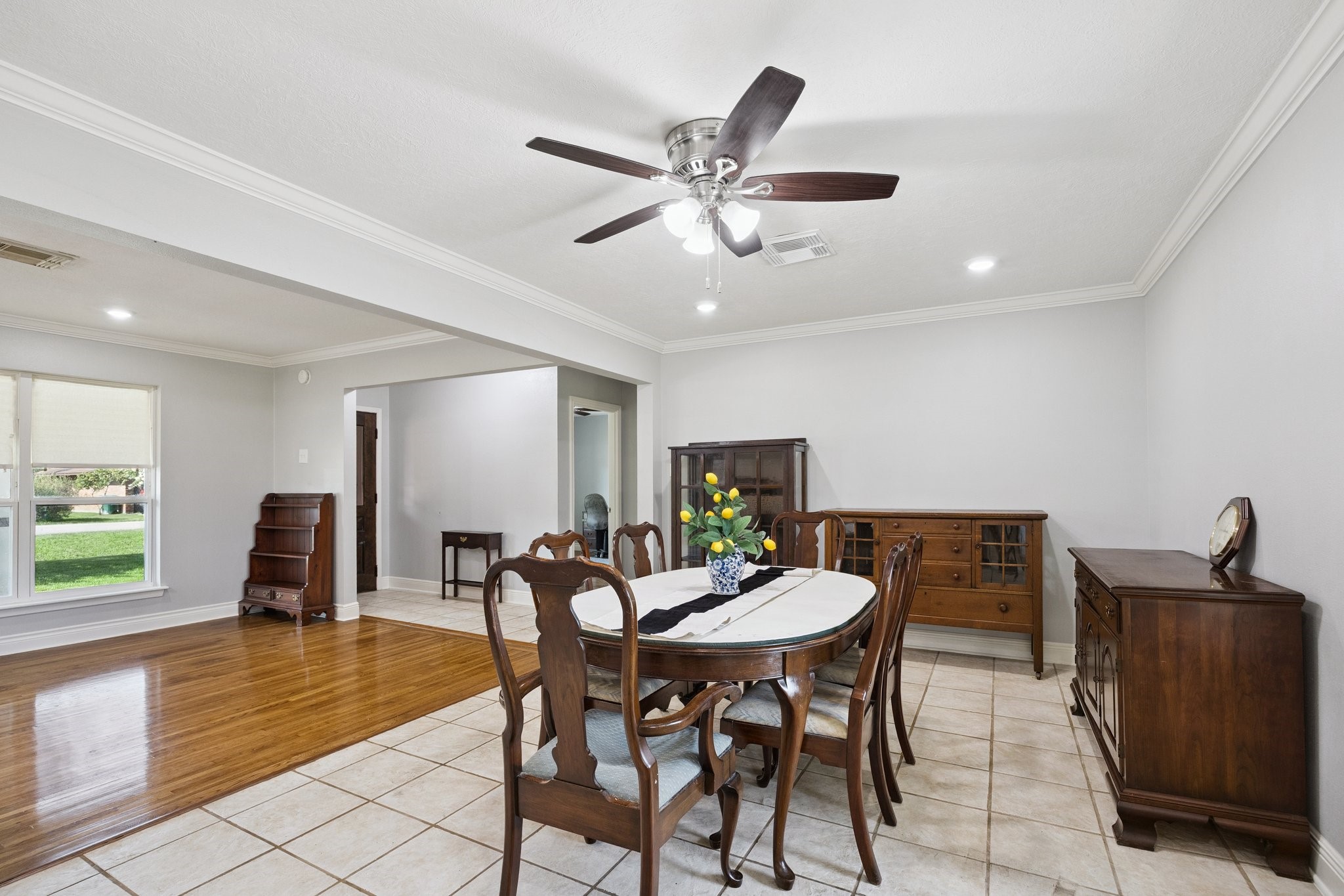 8911 Blankenship Drive Houston, TX 77080 - Photo 7 of 21 This photo features a bright dining area with a classic wooden dining set, tiled flooring, and a ceiling fan. The room opens to a living space with hardwood floors and large windows, providing ample natural light.